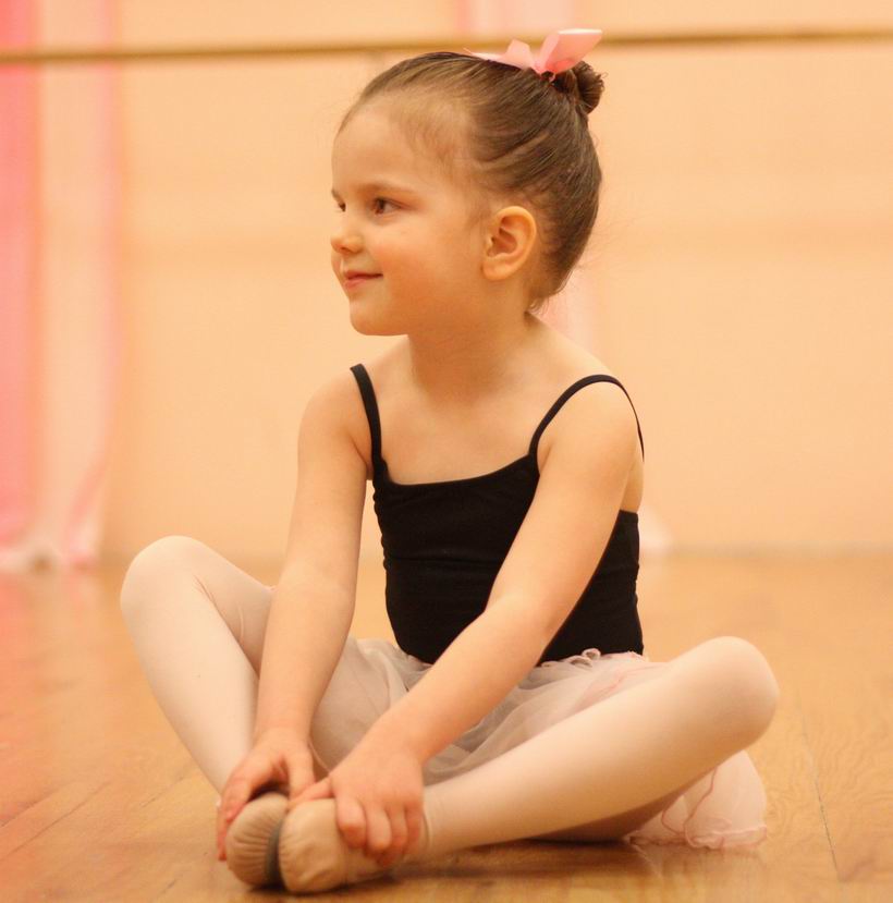 A young ballet student in pink stretching on the studio floor