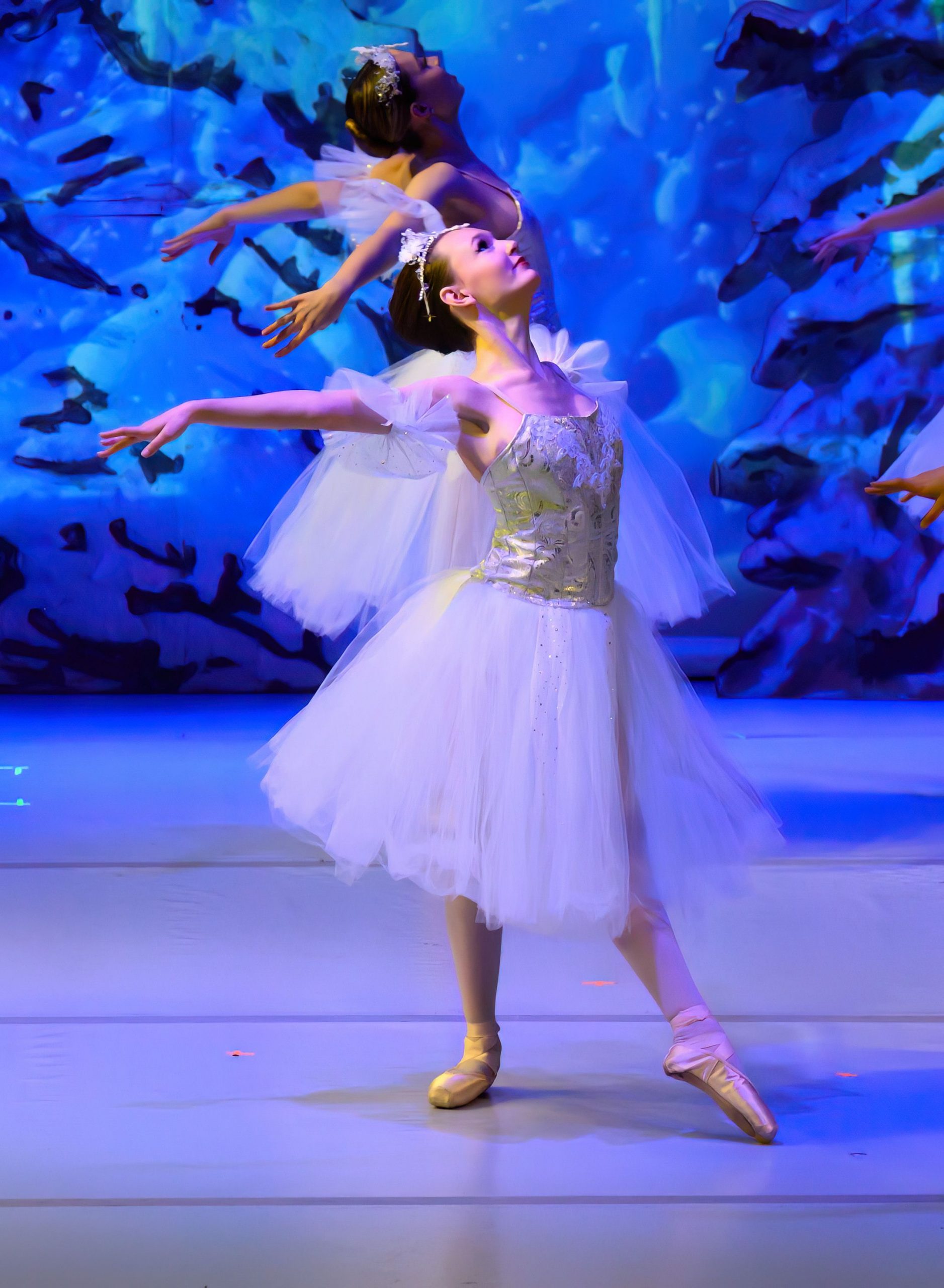 Two ballerinas in white tutus on stage, one en pointe